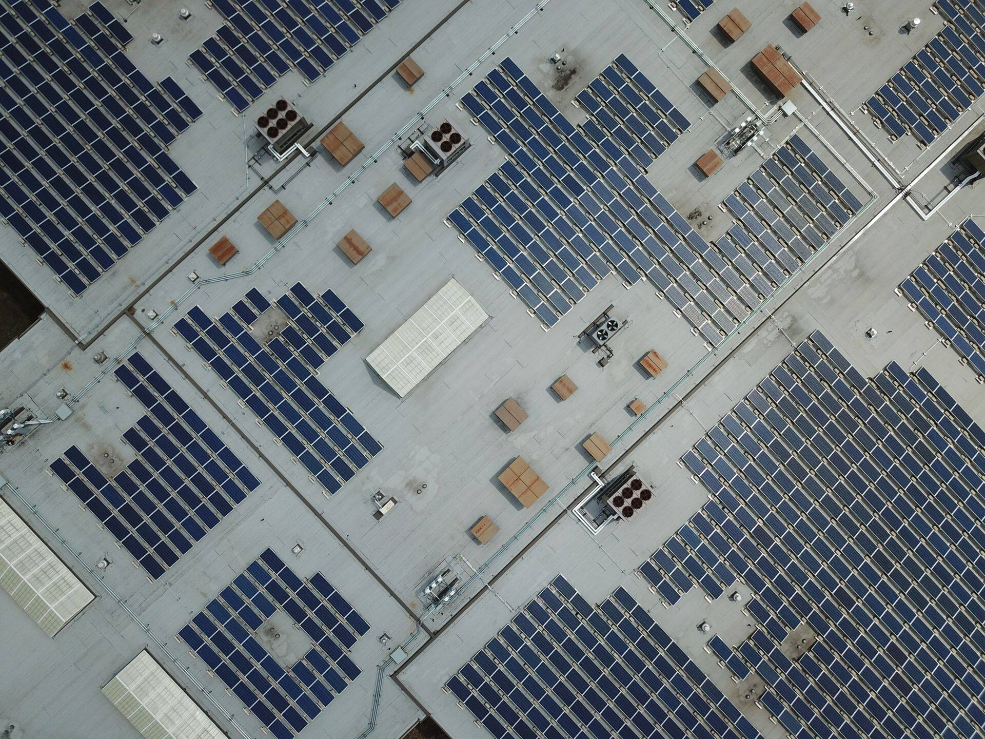 Vista aérea de telhado comercial com fileiras de painéis solares, laje e equipamentos de ar-condicionado